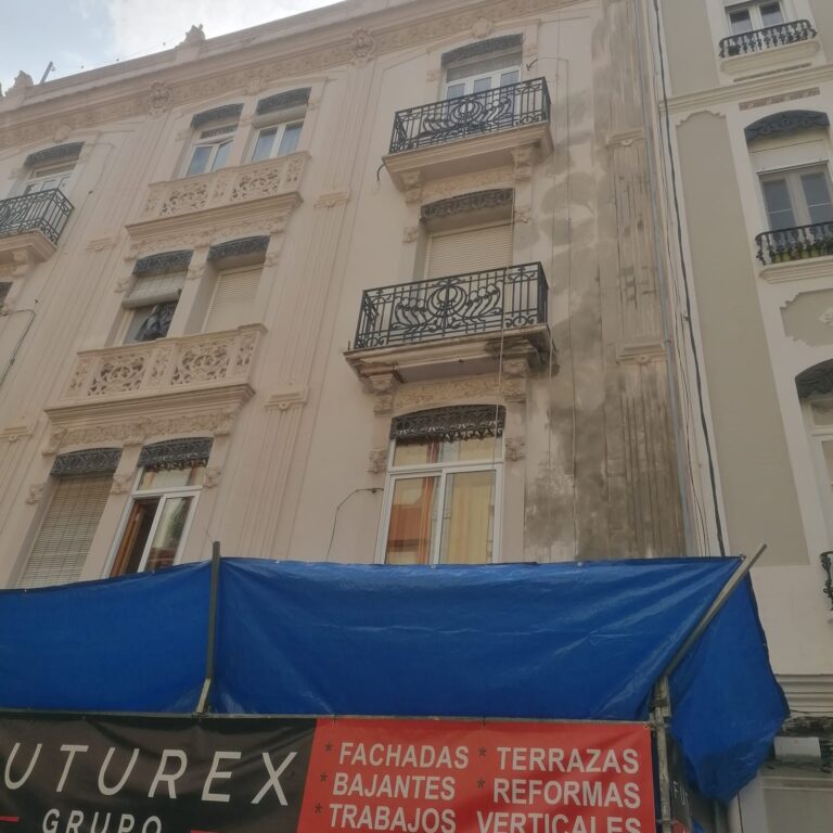 Fachada de edificio en proceso de restauración con lona azul en la parte baja